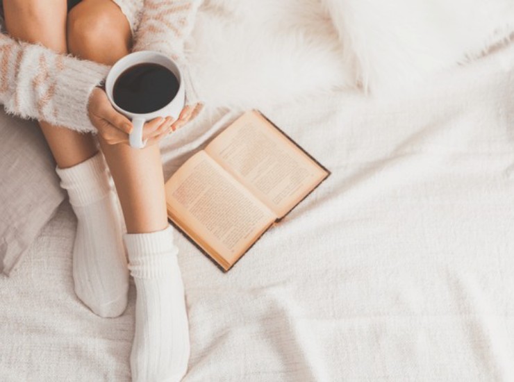 Donna legge e beve caffè a letto